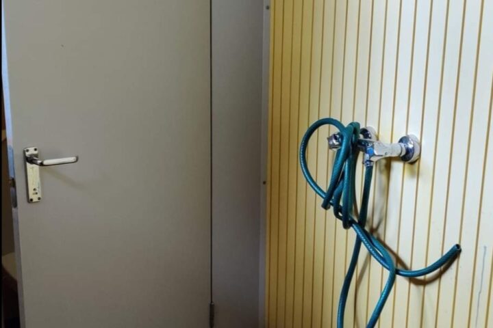 Hautausmaan vessa, jossa on puutarhaletkulla varustettu vesihana.