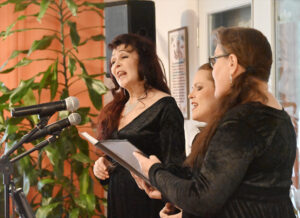 Kolme mustiin asuihin sonnustautunutta naishenkilöä laulamassa