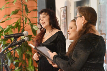 Kolme mustiin asuihin sonnustautunutta naishenkilöä laulamassa