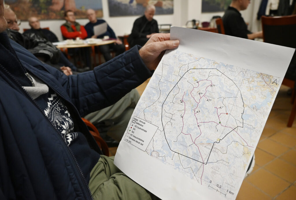 Karttakuva, joka on henkilön käsissä. Henkilöstä ei näy kuin käsivarsi ja takki. Taustalla muita henkilöitä.