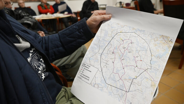 Karttakuva, joka on henkilön käsissä. Henkilöstä ei näy kuin käsivarsi ja takki. Taustalla muita henkilöitä.