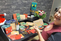 Pöytä jolla joulukortteja. Pöydän äärellä vasemmalla naishenkilö katsoo hymyillen kameraan