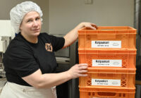 Henkilö, jolla leivontamyssy, musta t-paita ja esiliina, seisoo oranssien leipäkorien vierellä