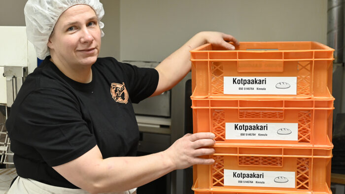 Henkilö, jolla leivontamyssy, musta t-paita ja esiliina, seisoo oranssien leipäkorien vierellä