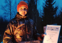 henkilö jolla yllään metsästysasu ja punainen pipo. Katsoo kameraan.