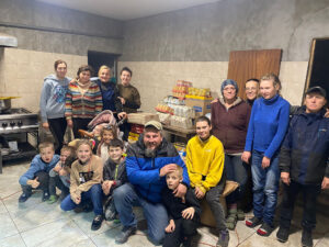 Joukko ihmisiä katsoo kameraan. He ovat sisätiloissa, osa seisten, osa polvillaan